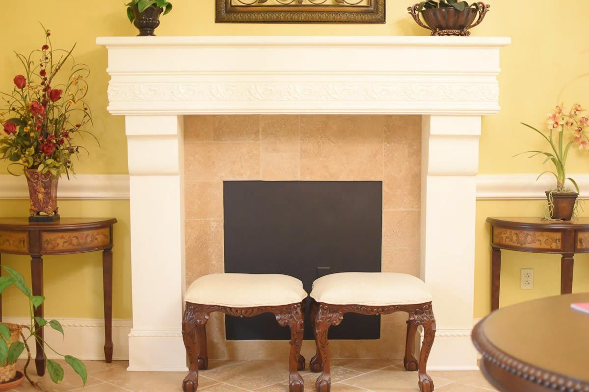 Fireplace with cream mantel, two stools, and tables with floral arrangements.
