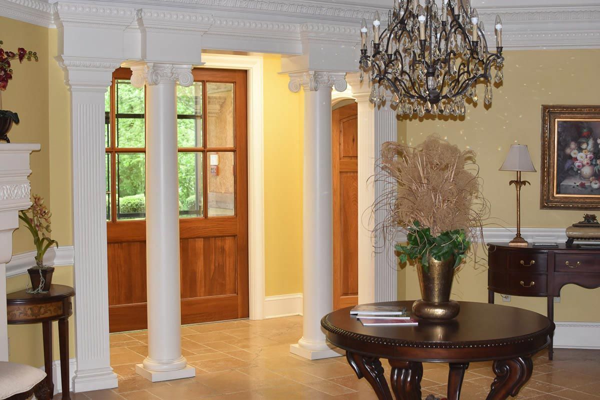 Elegant foyer with columns, wood doors, chandelier, round table, and a painting.