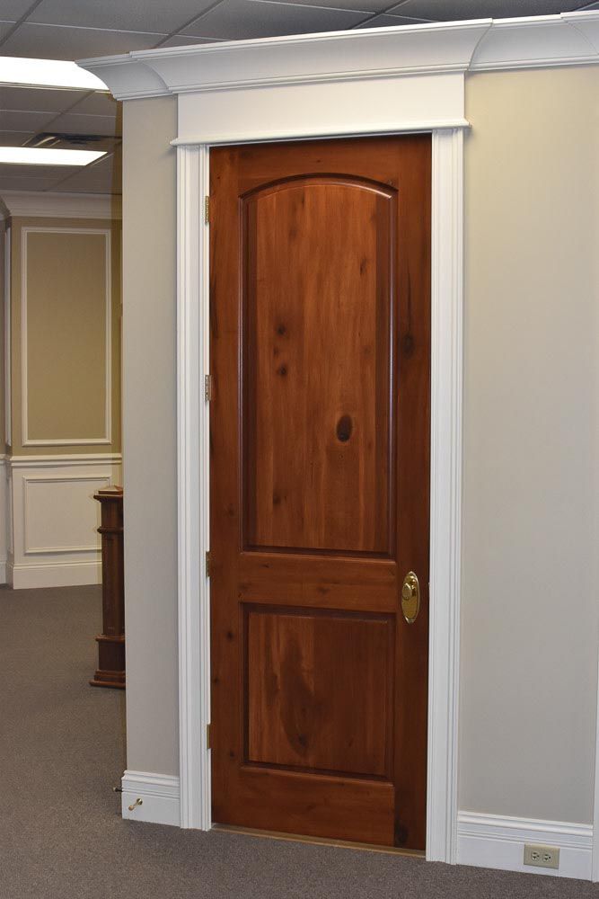 Wooden door with an arched top, surrounded by white trim, in a room with beige walls.