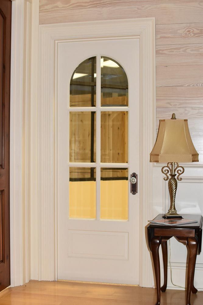 White arched-top door with glass panes, framed by white molding, next to a small table with a lamp.