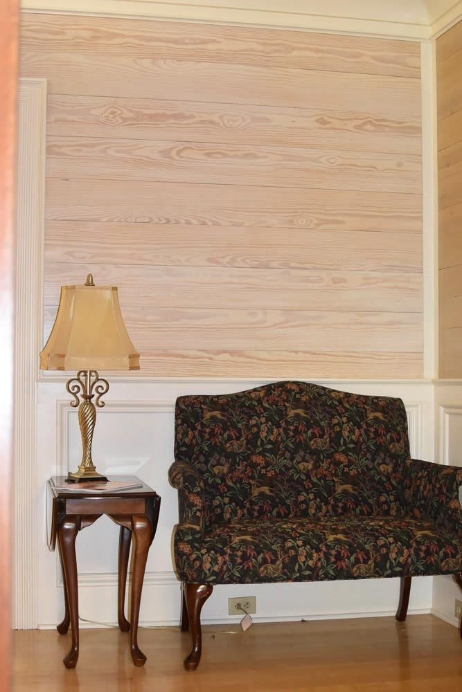 Couch, side table, and lamp in front of a wood-paneled wall, light wood floor and trim.