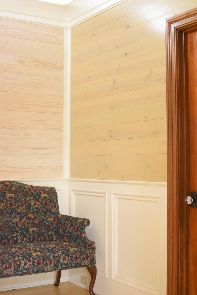 A small floral couch sits near panelled walls with light wood wallpaper, next to a closed brown door.