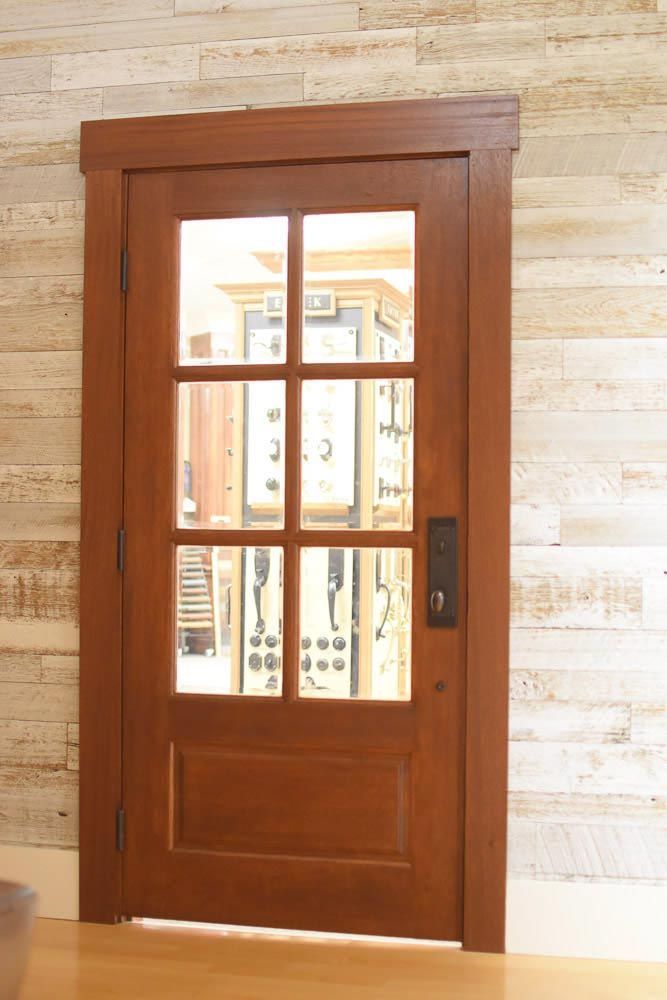 Wooden door with six glass panes and panel, brown trim, set against wood-paneled wall.