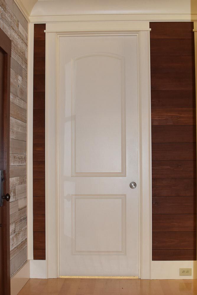 White door with an arched top, surrounded by dark wood paneling and white trim.