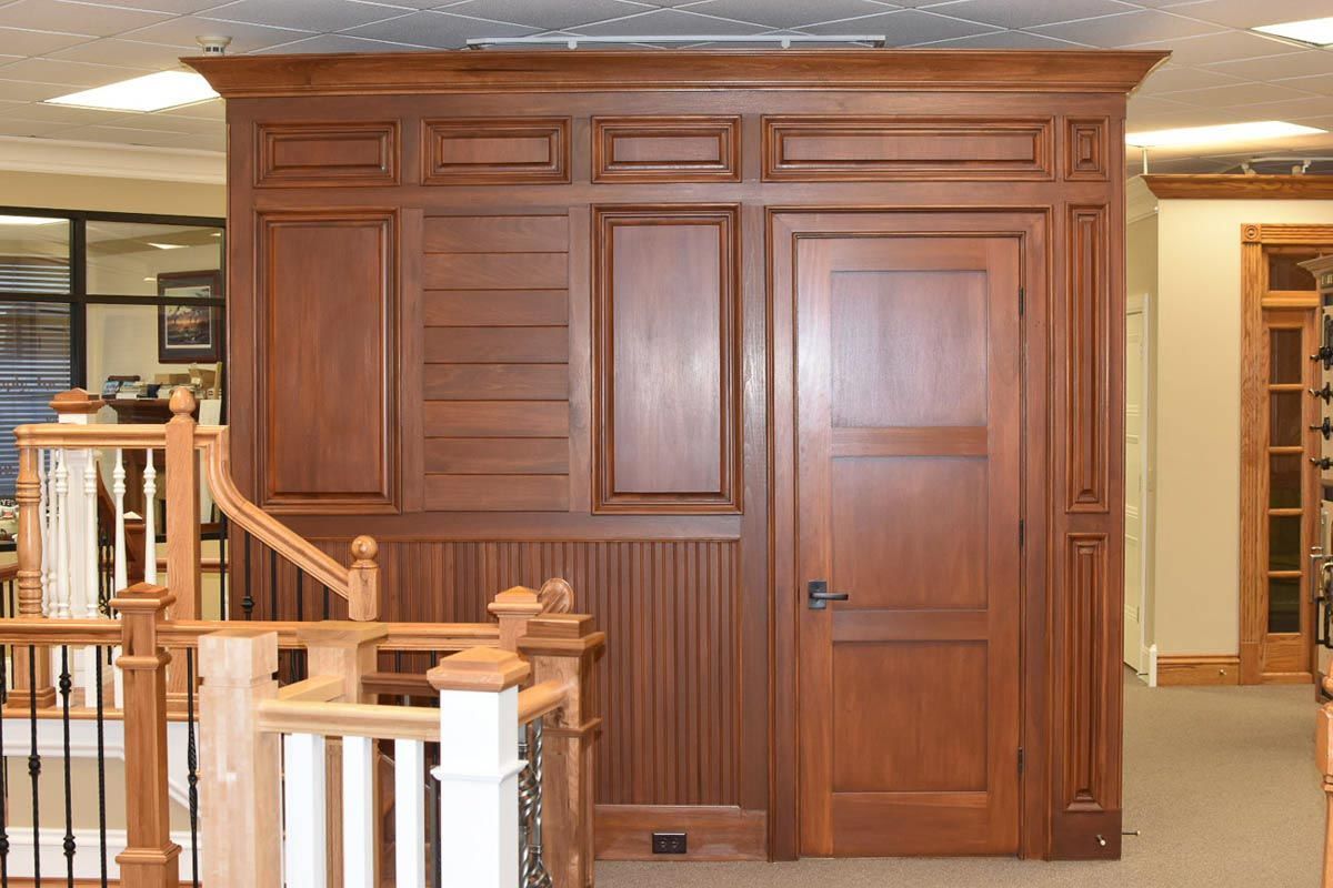 Wooden wall paneling with a door, decorative moldings, and staircase.