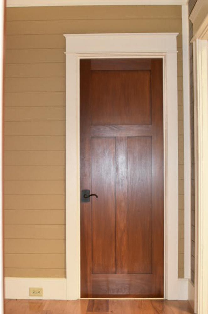 Brown wooden door with white trim, set in tan plank wall.