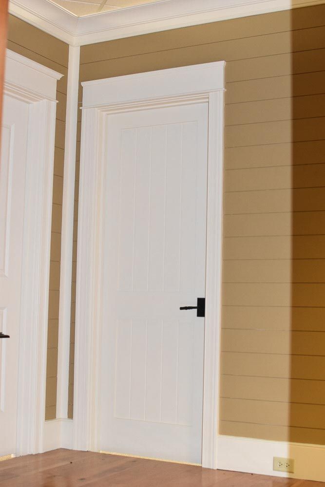 White door with black handle and trim in room with tan horizontal paneling.