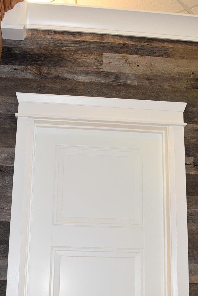White door with white trim against a wood-paneled wall, topped with crown molding.