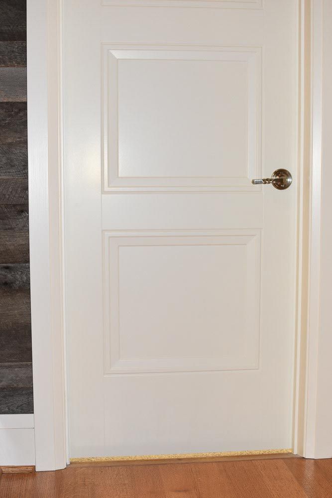 White two-panel door with silver handle, set in white door frame, over wooden floor.