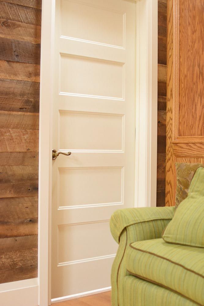 White paneled door in white trim, wooden walls on either side. Green armchair at right.