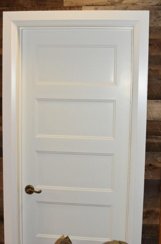 White four-panel door with gold handle and white trim, set against a wooden plank wall.