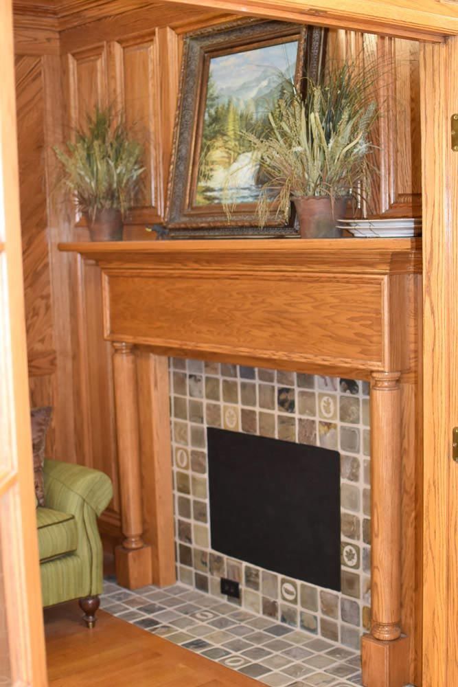 Fireplace with wooden mantel and tile surround, featuring artwork and plants.