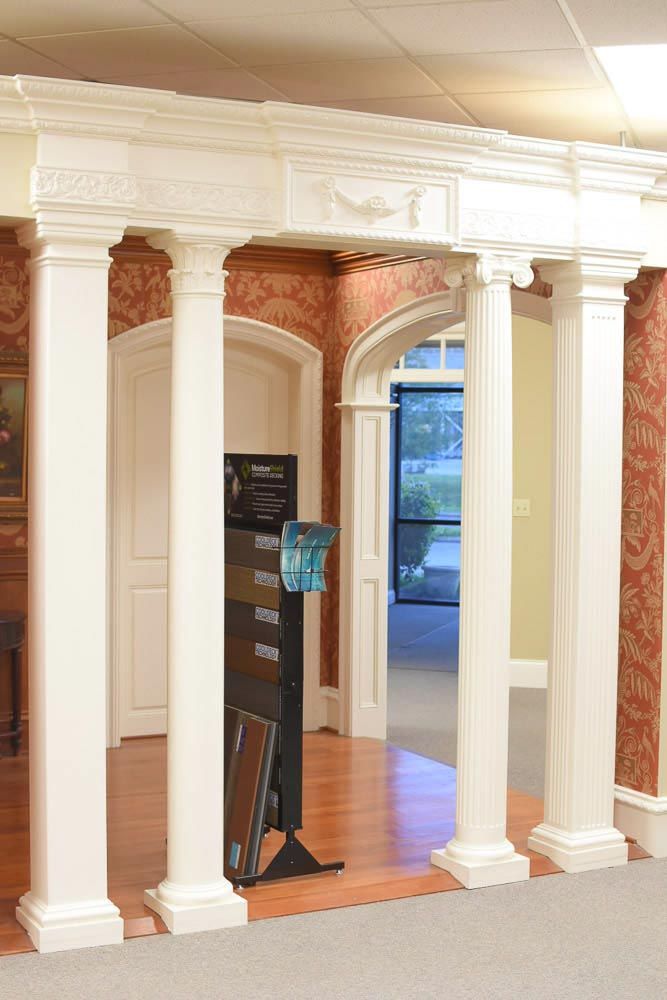 White columns and ornate molding frame doorways; display rack with samples on wood floor.
