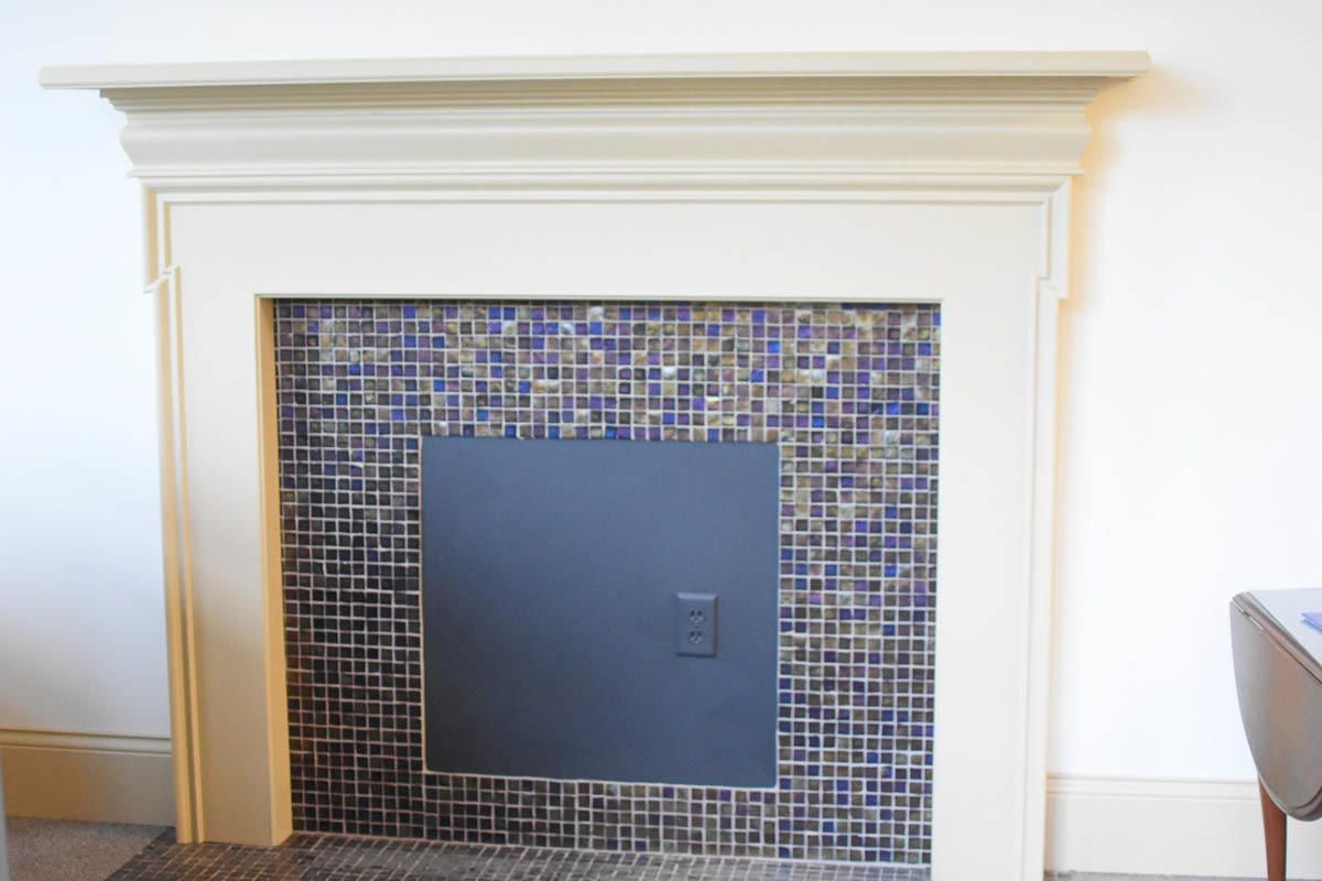 Fireplace with beige mantel, tiled interior (blue, gold, white), and black metal cover.