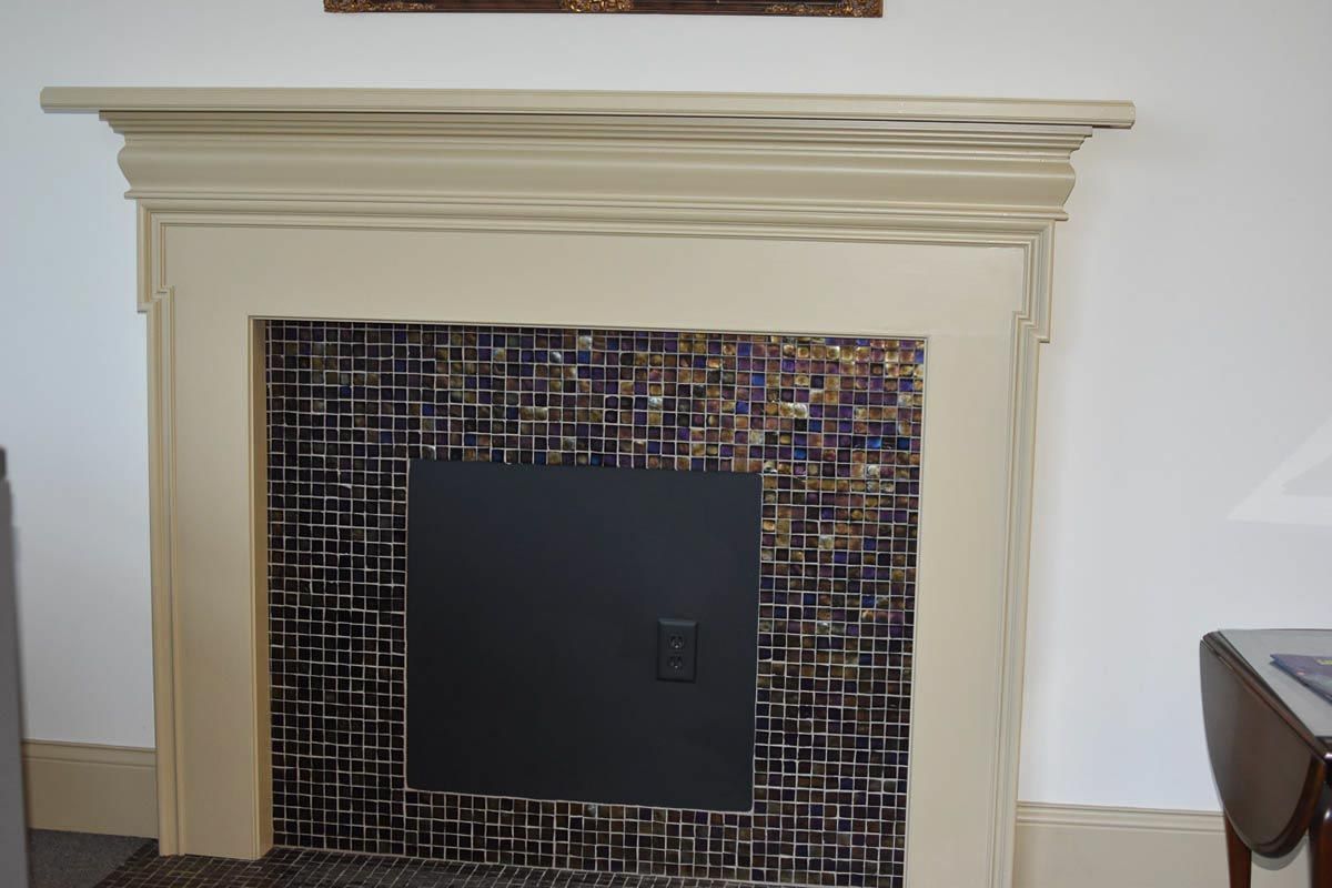 Fireplace with beige mantel, black firebox, and decorative tile surround.