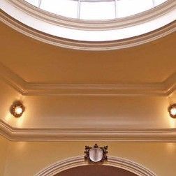 Beige interior ceiling with a circular skylight and ornate molding, wall sconces and a decorative crest.