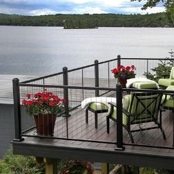 Deck overlooking a lake; black railings, potted red flowers, and green seating.