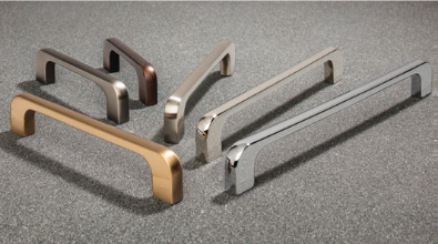 Various metal cabinet handles in bronze, silver, and copper tones, arranged on a gray surface.