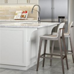 White kitchen island with marble countertop, two bar stools, stainless steel fridge.