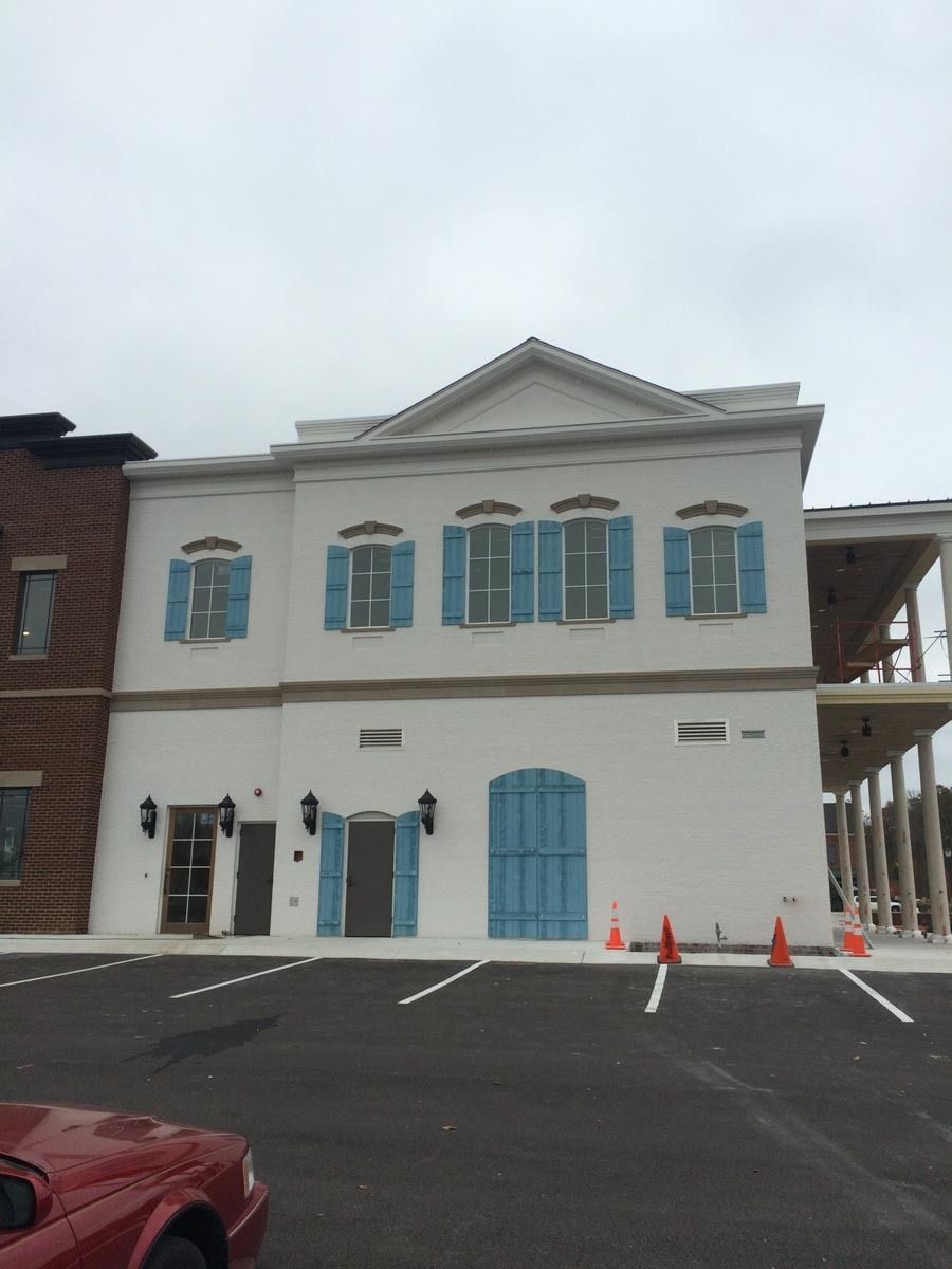White building with blue shutters and door, under construction with an overcast sky.