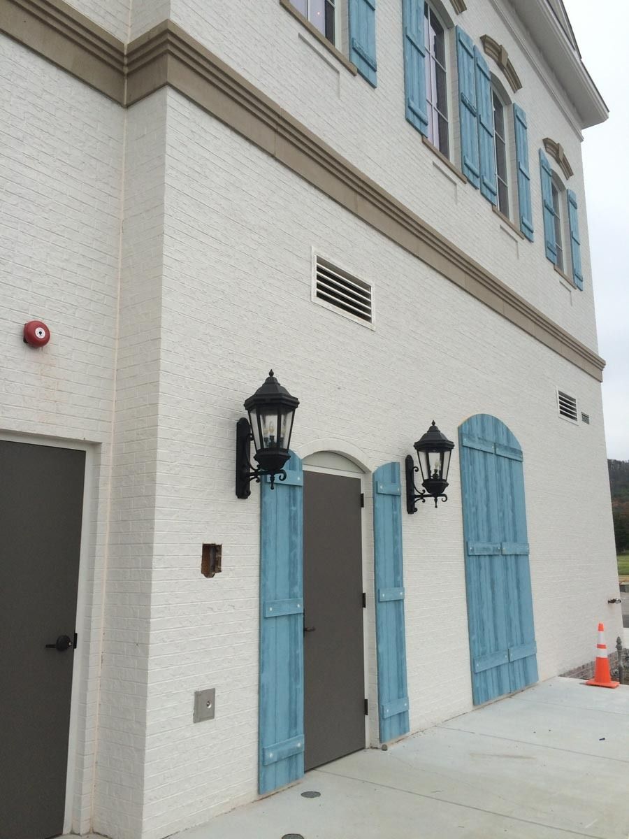 White brick building with blue shutters, grey door, and black lanterns.