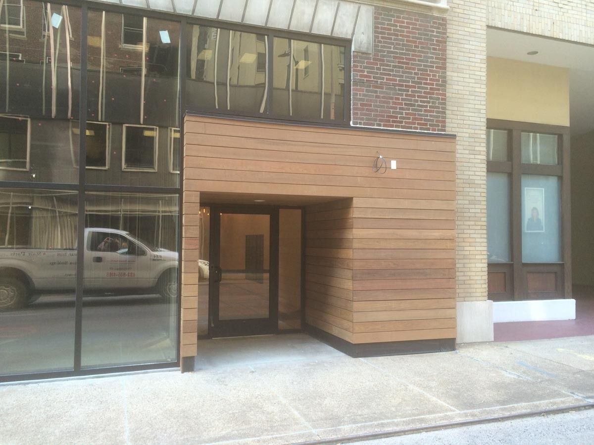 Entrance to a building with glass windows, brown wood facade, and a truck reflected in the glass.