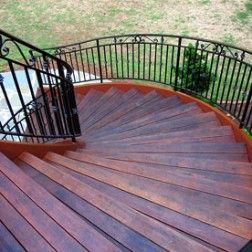Curving wooden staircase with black metal railing, leading to a grassy area.