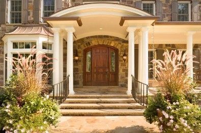 Stone facade home with arched entry, wooden door, steps, and potted plants.