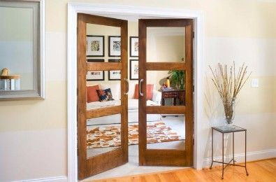 Open wooden interior doors with glass panes, leading to a living room with art, a rug, and a couch.