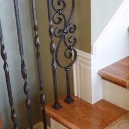 Dark metal stair railing with ornate scroll design and wooden steps.