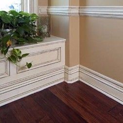 Corner of room with dark wood floor, tan wall, white molding and chest, and potted plant.