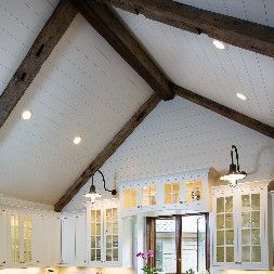 White kitchen with a vaulted ceiling, wood beams, and recessed lighting.
