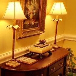 Two lamps on a wooden table, with a painting above. Yellow wall.