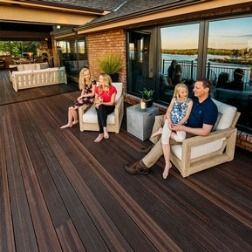 Family relaxing on a wooden deck with view of water, sun setting.