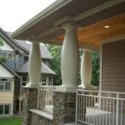 Beige porch columns with a stone base supporting a brown overhang, with a white railing.