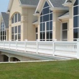 Beige mansion with arched windows, a white balcony, and bridge over a green lawn.