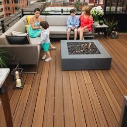 Rooftop deck with seating, fire pit, and family. Wood flooring, plants, and city view.