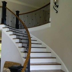 Curved staircase with wooden handrail, black metal spindles, and white risers.