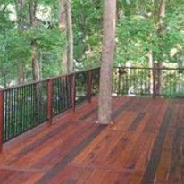 Wooden deck with a tree growing through it, surrounded by black railing in a wooded setting.