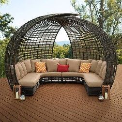 Woven, dome-shaped outdoor couch with beige cushions and decorative pillows on a wooden deck.