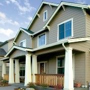 Beige house with white columns, windows, and dark green roof against a blue sky.