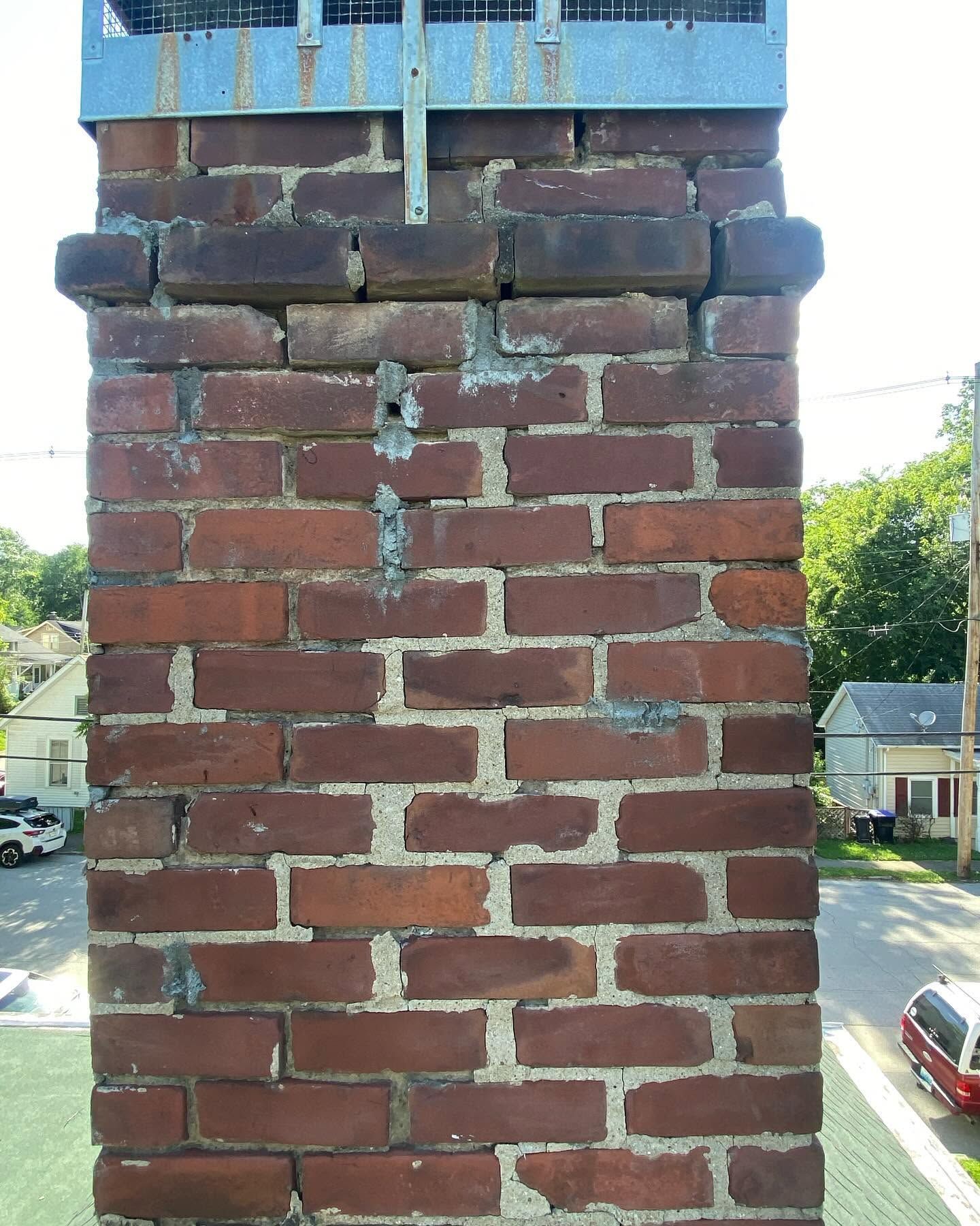 Cracked red brick chimney with crumbling mortar against a suburban street background