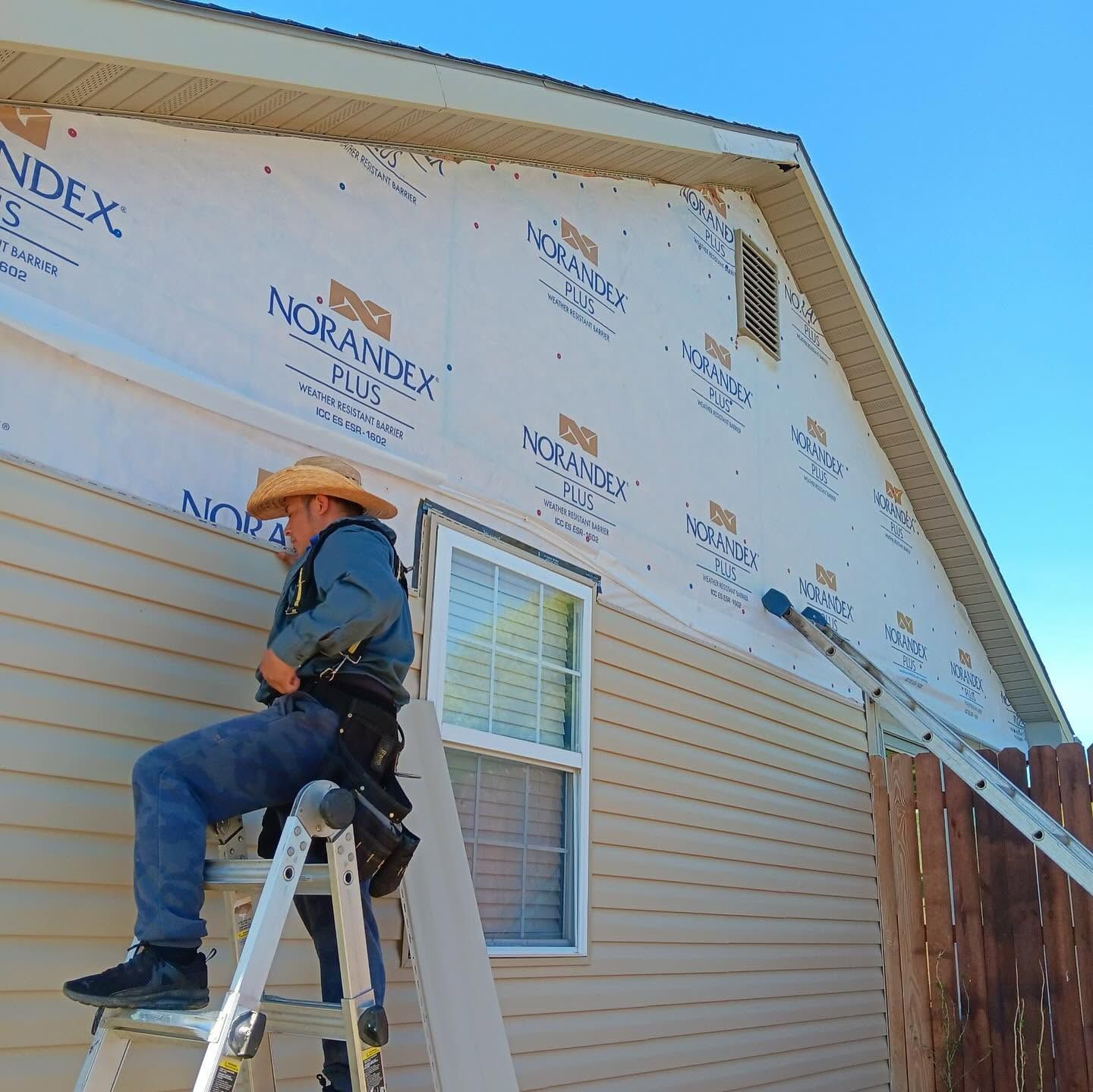 Worker on ladder installing house siding under a blue sky