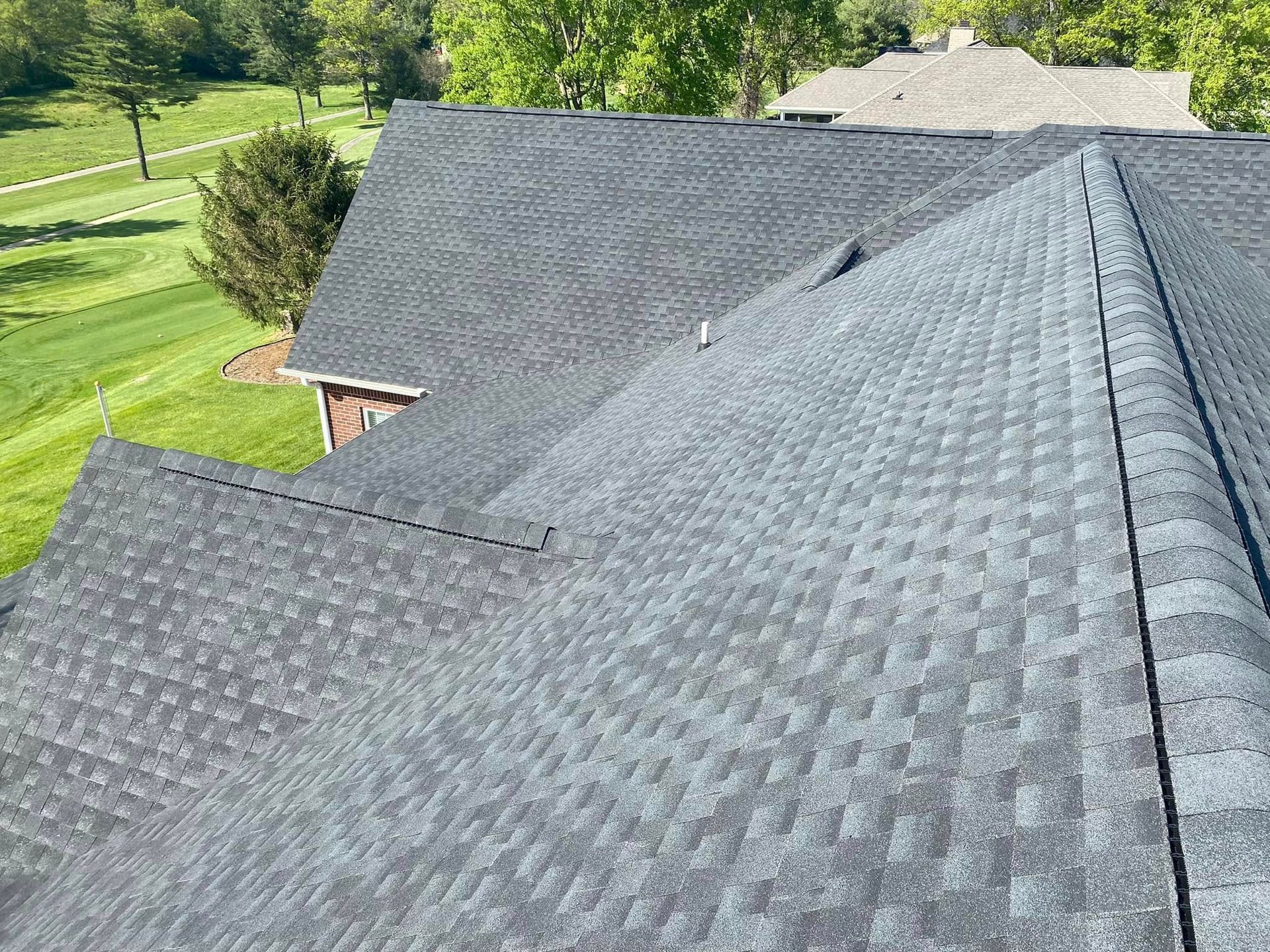 Gray shingled roof on a house beside a green lawn and trees