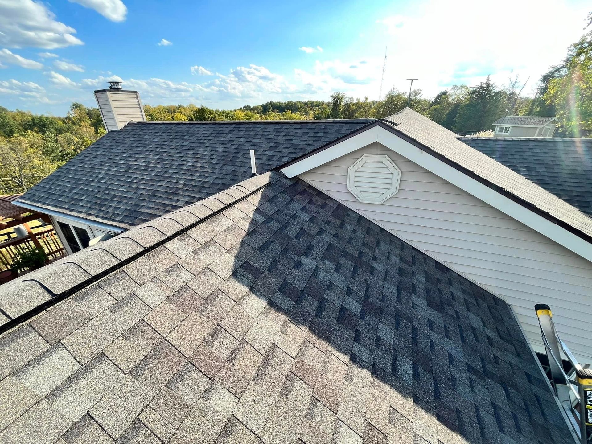Rooftop with gray shingles and white siding, showing a bright sunlit suburban neighborhood beyond.