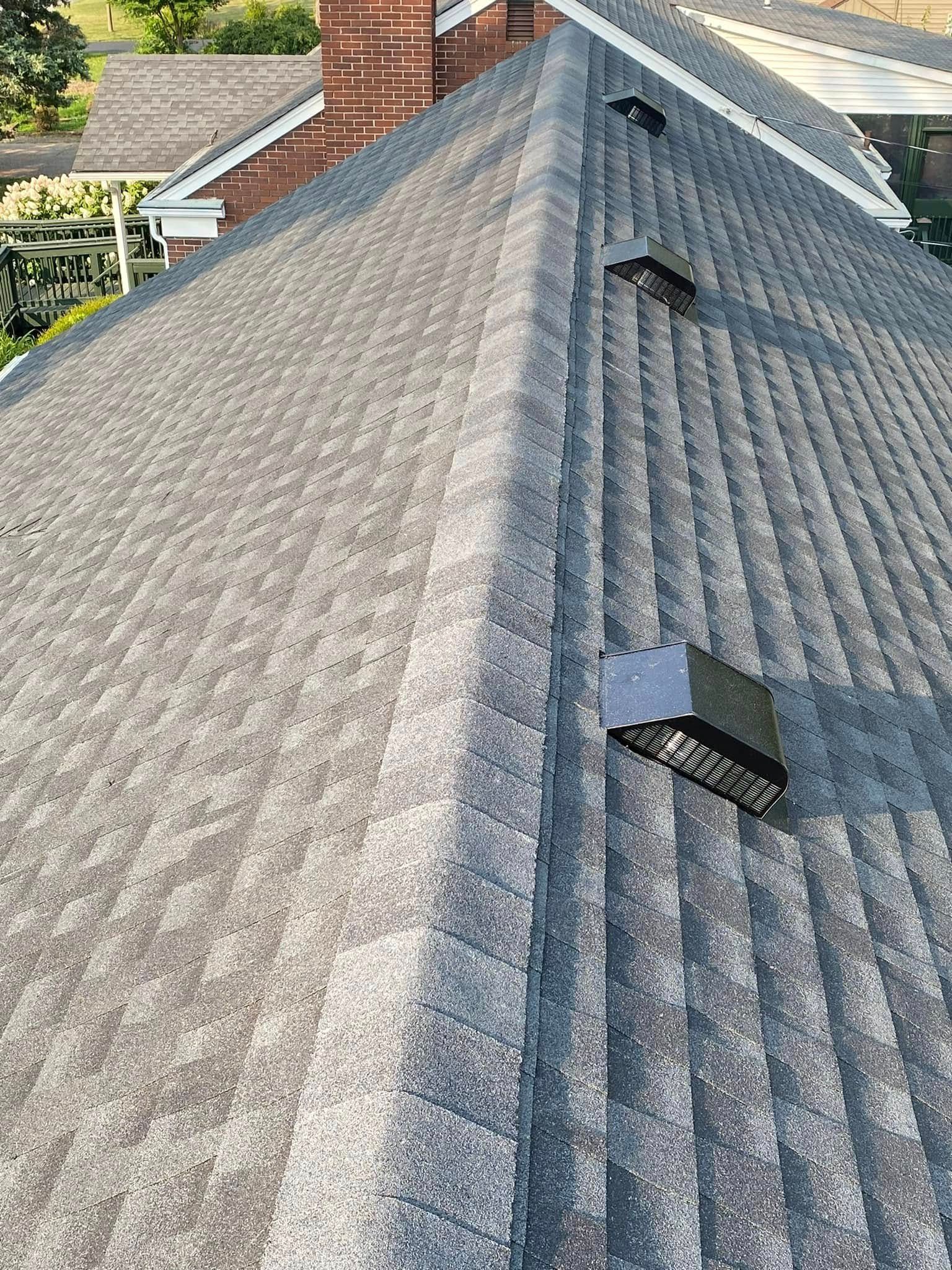 Gray shingled roof with two vent pipes and a brick chimney under daylight