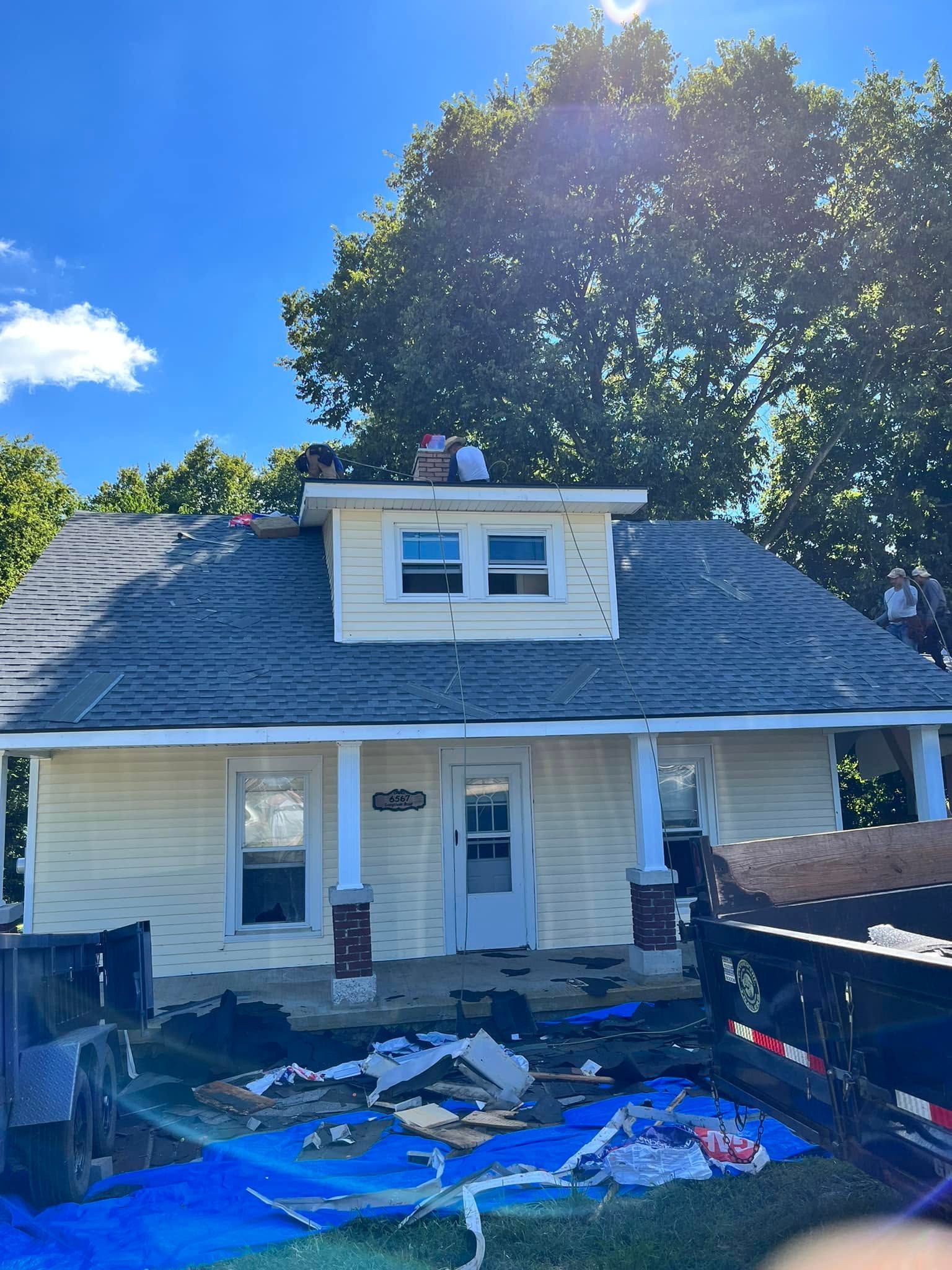 House exterior with white siding and blue roof tarps during repairs, with debris in the front yard.