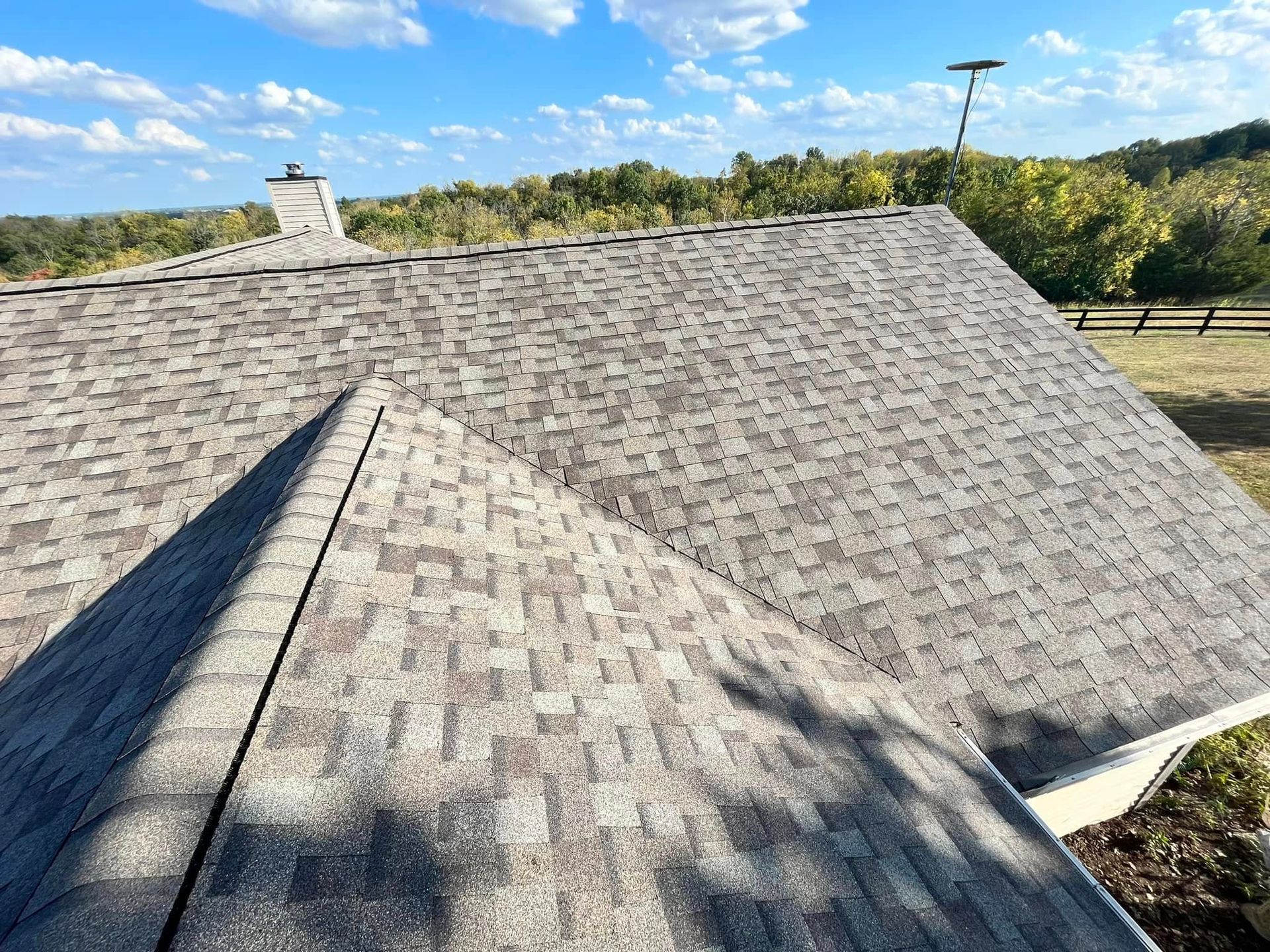 Gray shingle roof on a house with a chimney, seen from above against a wooded background