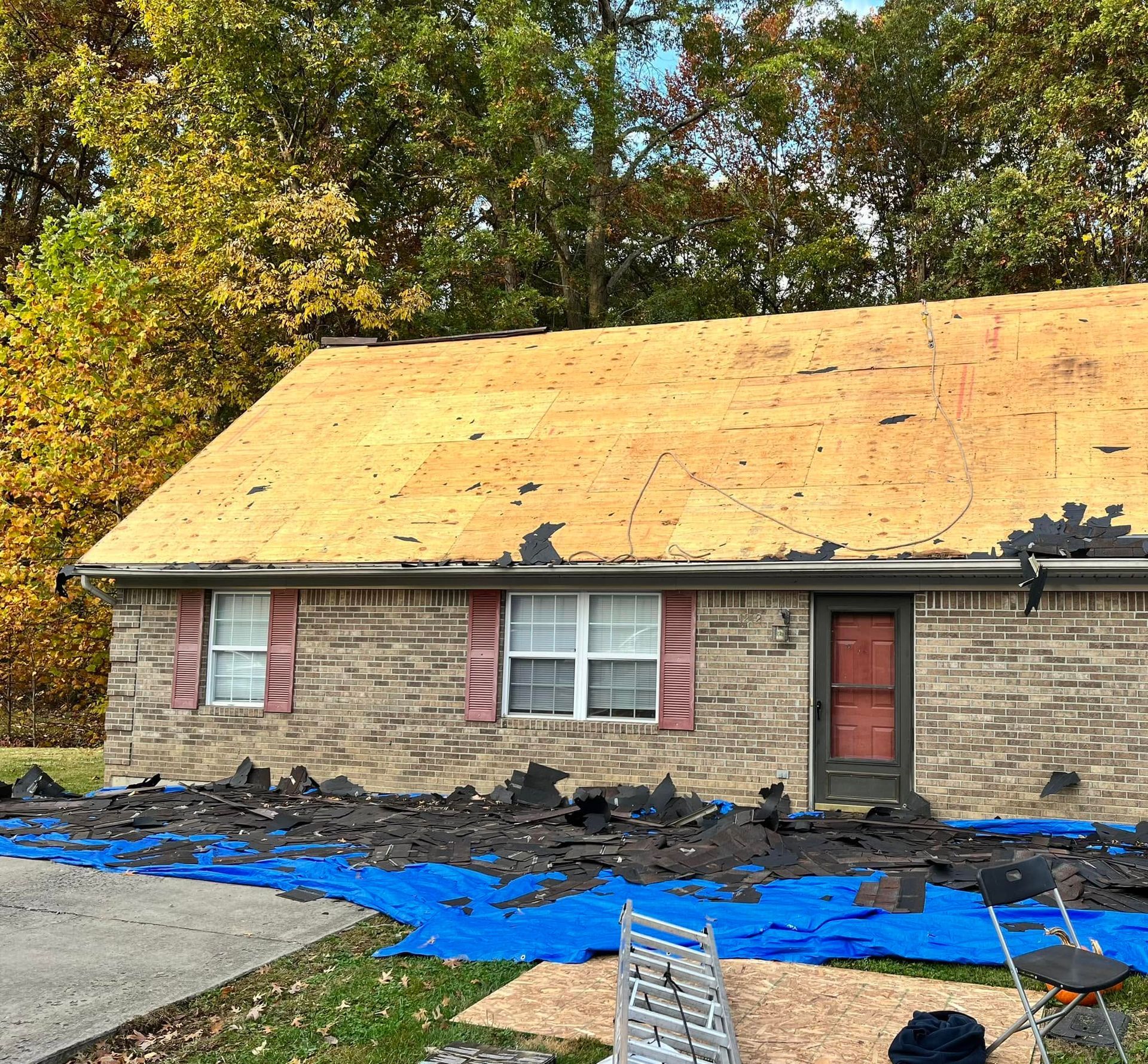 House with new yellow roof under construction, stone exterior, and blue tarps covering debris in front yard