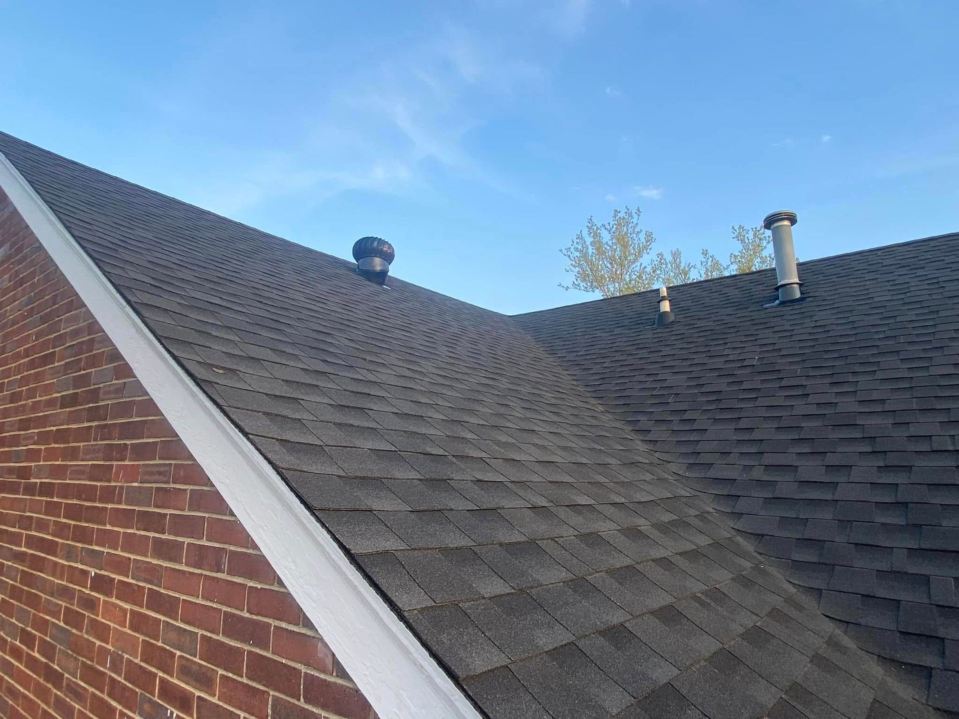 Two dark shingled roof slopes with a brick wall and white trim under a blue sky.